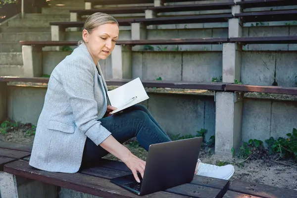 Dışarıda dizüstü bilgisayarı olan bir kadın. Serbest meslek anlayışı, çevrimiçi eğitim veya iş planlaması.