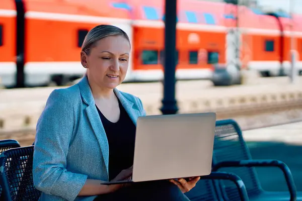 Tren istasyonunda dizüstü bilgisayarla uzaktan çalışan kendine güvenen bir kadın, seyahat zamanını iş için kullanıyor..               