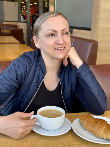 Kahve ve kruvasan içen bir kadın. Pozitif ruh hali ve doğal ışık ile günlük kahvaltı anı.