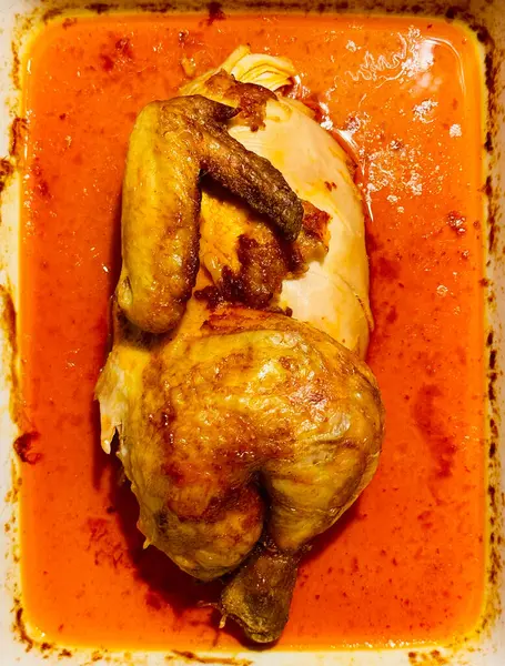 Baharatlı kırmızı soslu tam kızarmış tavuk. Kavrulmuş tavuğun tepeden tırnağa görüntüsü canlı kırmızı sosla dolu bir kabın içinde servis ediliyor.. 