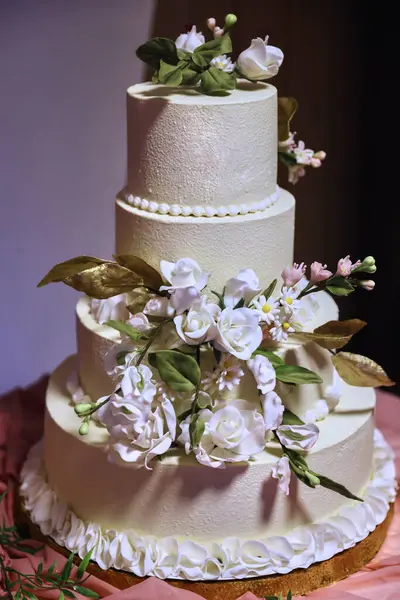 Şeker çiçekleri ve altın yapraklarla süslenmiş zarif, beyaz katlı düğün pastası. Düğünler, yıldönümleri ya da lüks etkinlikler için mükemmel lüks bir tatlı süsü..