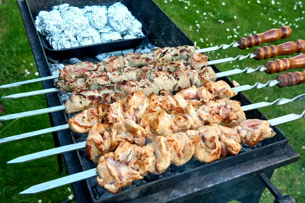 Salamura edilmiş domuz eti ve tavuk şişleri, arka bahçede folyoyla sarılmış patateslerle ızgara yapıyor. Klasik barbekü sahnesi, açık hava toplantıları ve yaz partileri için mükemmel..