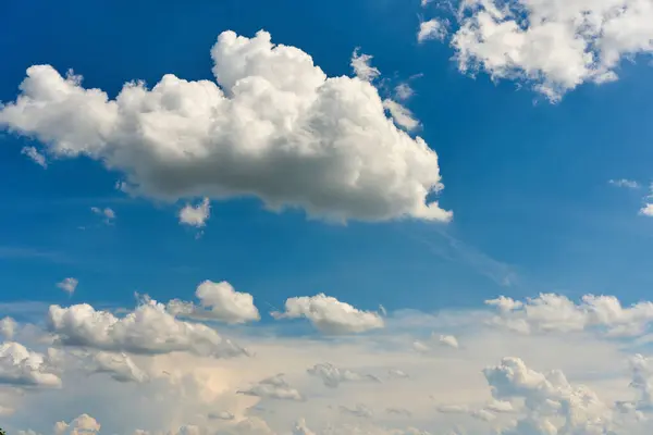 Yumuşak kümülüs bulutlarıyla dolu sakin bir gökyüzü canlı mavi bir arkaplanda huzur içinde sürükleniyor..