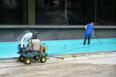 Bir işçi profesyonel ekipmanlarla havuzu temizliyor, şehrin simgesel kamusal alanı için el değmemiş su kalitesini sağlıyor..                               