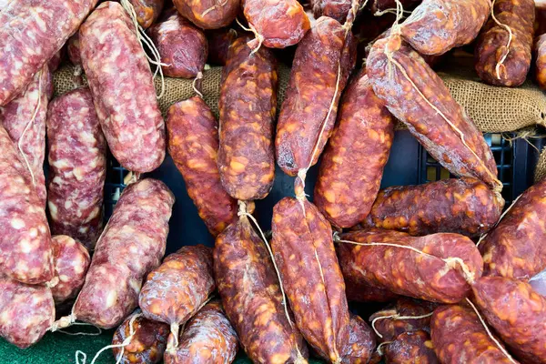 Yerel bir pazarda sergilenen geleneksel kurutulmuş sosis çeşitleri, zengin dokuları ve koyu kırmızımsı renkleri gösteriyor.
