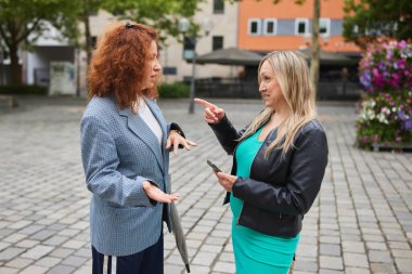 İki kadın hareketli bir sokak sohbetine girişiyor, biri anlamlı bir şekilde el kol hareketi yaparken diğeri ise bir anlık animasyon diyalog ve bağlantı kurma anı ile işaret ediyor..