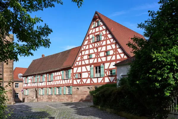 Güneşli bir bahar gününde ağaçların çerçevelediği sessiz bir kaldırım taşı caddesinde yeşil kepenkleri olan geleneksel yarı keresteli bir bina..