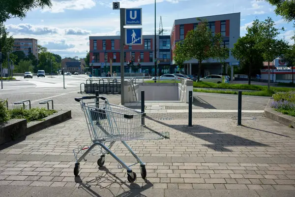 Boş bir alışveriş arabası Stadthalle metro istasyonunun girişine yakın modern binalar ve öğleden sonra güneşli sakin bir şehir caddesinde bırakılmış..
