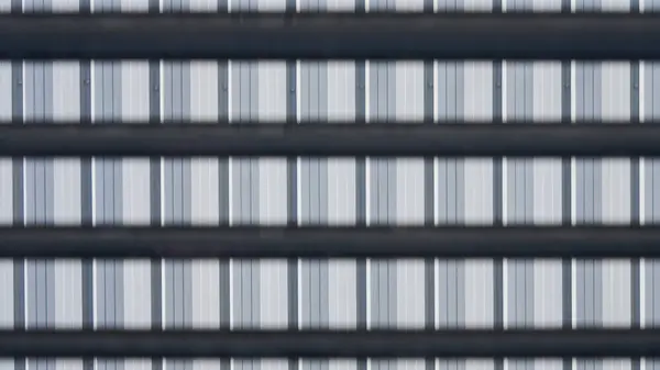 Tekrarlayan dikey çizgileri ve yatay siyah çubukları olan metal bir cepheye yakın plan. Geometrik çizgileri ve minimal renk karşıtlığı olan soyut sanayi deseni.