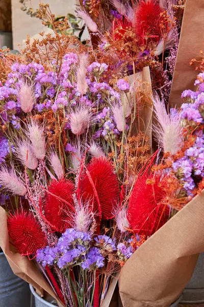 Kurumuş çiçekler, çarpıcı kırmızı devedikeni, yumuşak pembe otlar, ve narin mor çiçekler, kahverengi kağıtta düzenlenmiş canlı bir kırsal ekran için.