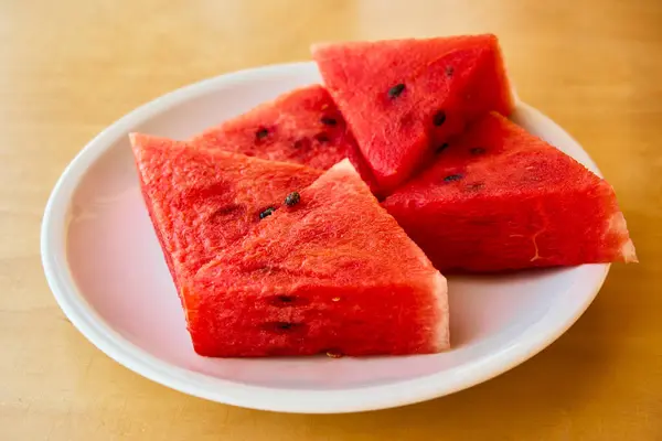 Beyaz tabakta taze dilimlenmiş karpuz. Yaz tatlısı olarak sunulan sulu kırmızı meyve, sağlıklı ve ferahlatıcı atıştırmalık..