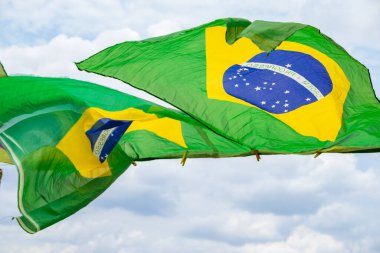 Rüzgarda sallanan bazı Brezilya bayrakları, çamaşır ipinde sergileniyor. Arka planda bulutlu bir gökyüzü var..