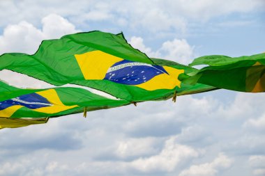 Rüzgarda sallanan bazı Brezilya bayrakları, çamaşır ipinde sergileniyor. Arka planda bulutlu bir gökyüzü var..
