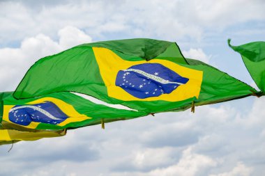 Rüzgarda sallanan bazı Brezilya bayrakları, çamaşır ipinde sergileniyor. Arka planda bulutlu bir gökyüzü var..
