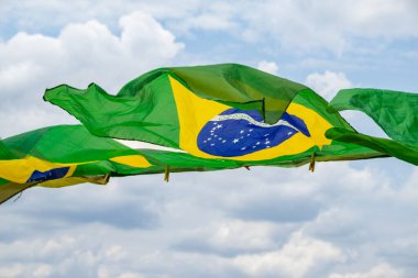 Rüzgarda sallanan bazı Brezilya bayrakları, çamaşır ipinde sergileniyor. Arka planda bulutlu bir gökyüzü var..