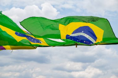 Rüzgarda sallanan bazı Brezilya bayrakları, çamaşır ipinde sergileniyor. Arka planda bulutlu bir gökyüzü var..