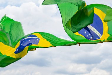 Rüzgarda sallanan bazı Brezilya bayrakları, çamaşır ipinde sergileniyor. Arka planda bulutlu bir gökyüzü var..