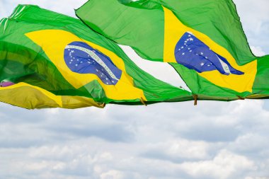 Rüzgarda sallanan bazı Brezilya bayrakları, çamaşır ipinde sergileniyor. Arka planda bulutlu bir gökyüzü var..