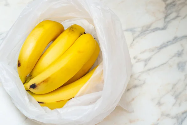 A bunch of bananas in a plastic bag on the table.