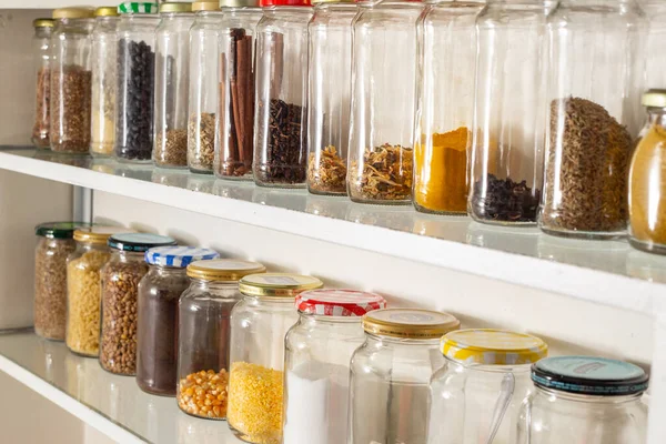 Side view of some glass containers with bulk food on a wall shelf. Reuse of glass packaging for industrialized products.