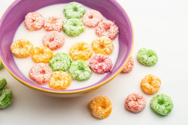Bowl with colored breakfast cereals in milk, ready to eat and some cereals lying on the table. Image in horizontal format.
