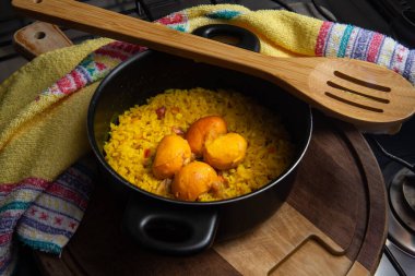 Pequi 'li siyah bir tava, tahta bir kaşık ve tahta bir tahtanın üzerinde bulaşık havlusu. Tipik bir Brezilya yemeği..