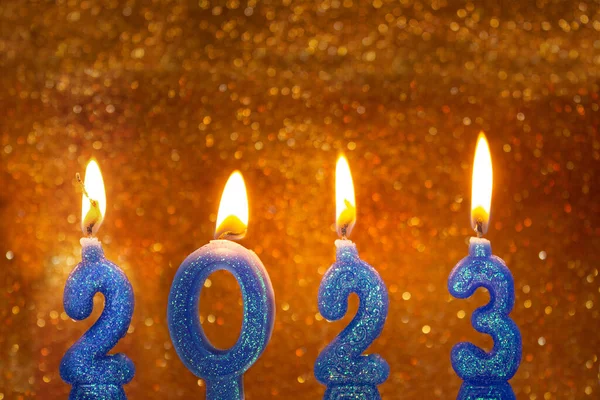 Four candles lit with the number two thousand and twenty-three, with a golden and shiny background.