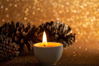 Noel süslemeleri, biraz kozalak ve parlak altın arkaplanda yanan bir mum..