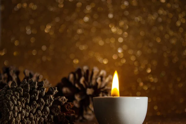 クリスマスの装飾 明るい金の背景にいくつかの松のコーンとライトアップキャンドル — ストック写真