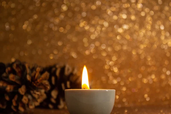 Karácsonyi Dekorációk Néhány Fenyőtoboz Egy Meggyújtott Gyertya Fényes Arany Háttér — Stock Fotó