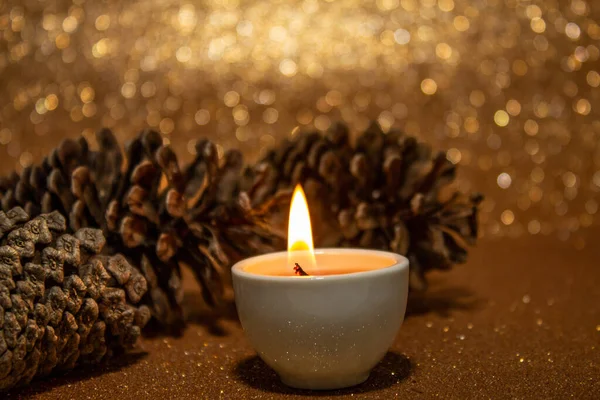 クリスマスの装飾 明るい金の背景にいくつかの松のコーンとライトアップキャンドル — ストック写真