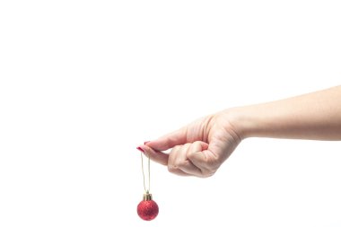 Kırmızı tırnaklı bir kadın eli, beyaz arka planda kırmızı bir Noel topu tutuyor..