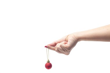 Kırmızı tırnaklı bir kadın eli, beyaz arka planda kırmızı bir Noel topu tutuyor..