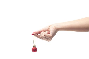 Kırmızı tırnaklı bir kadın eli, beyaz arka planda kırmızı bir Noel topu tutuyor..
