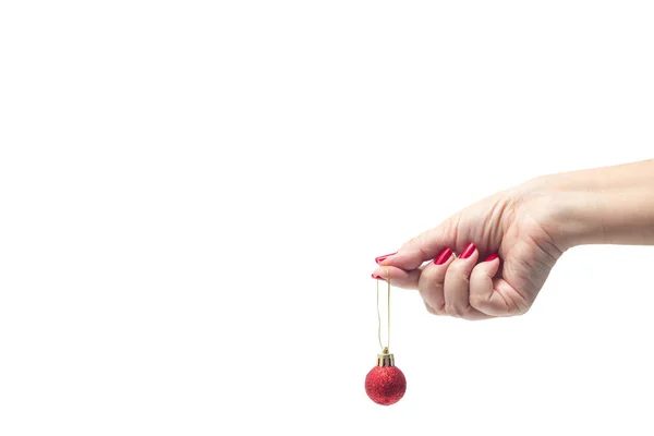 A female hand, with red painted nails, holding a red Christmas ball against a white background.
