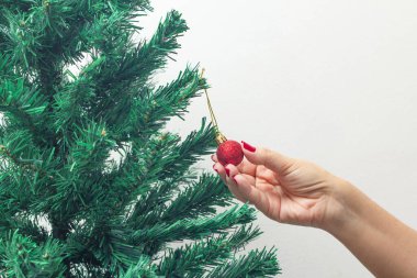 Kırmızı tırnaklı kadın eli, kırmızı bir top tutuyor, Noel ağacını birleştiriyor..