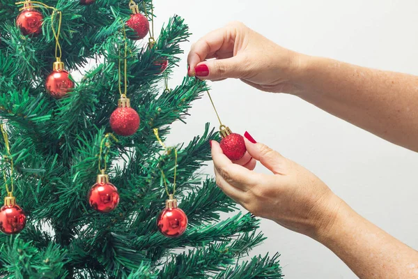 Female hands with red painted nails, holding a red ball, assembling the Christmas tree.