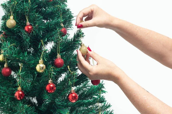 Female hands with red painted nails, holding a red ball, assembling the Christmas tree.