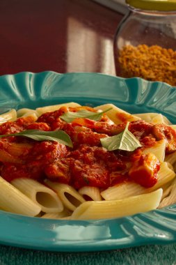 Parlak yeşil bir tabakla domates soslu makarna ve parlak bir yüzeyde fesleğen yaprakları..