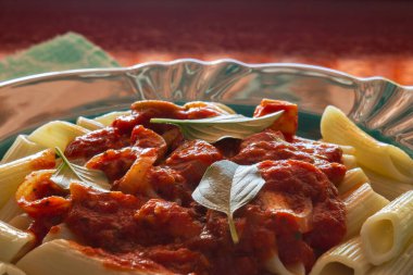 Parlak yeşil bir tabağa yakın domates soslu makarna ve parlak bir yüzeyde fesleğen yapraklarıyla..