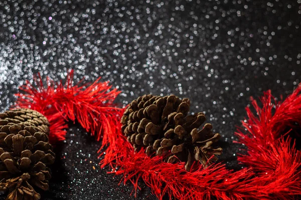 光沢のある黒い背景に松の実がある赤いガーランド — ストック写真