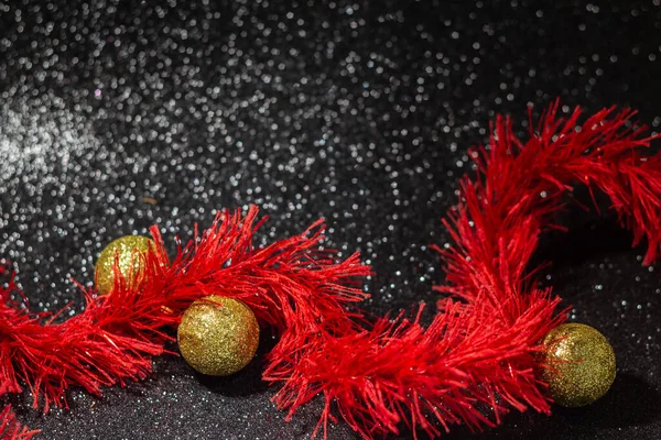 キラキラと黒の背景にいくつかの黄金のクリスマスの泡と赤いガーランド — ストック写真