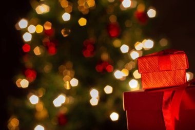 İki hediye kutusu, kırmızı, kurdeleli, arkasında Noel ağacı olan..