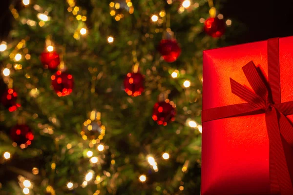 Ένα Κουτί Δώρου Κόκκινο Μια Κορδέλα Τόξο Ένα Χριστουγεννιάτικο Δέντρο — Φωτογραφία Αρχείου