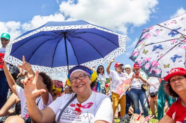 Yerde oturan iki kadın, kendilerini sıcak güneşten renkli şemsiyelerle koruyorlar. Fotoğraf Başkan Lula 'nın göreve başlama partisinde çekildi..