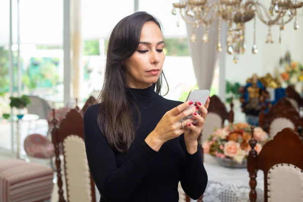 A young woman, wearing a long-sleeved black blouse, is dialing on her cell phone.