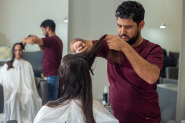 A hairdresser separating a lock of a client's hair to cut. Reflection of the action in the mirror.
