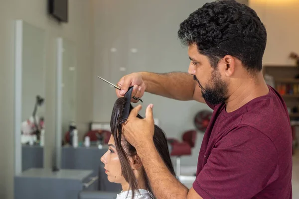 A hairdresser separating a lock of a client\'s hair to cut.