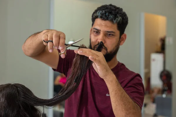 A hairdresser cutting the ends of a client's hair using scissors.