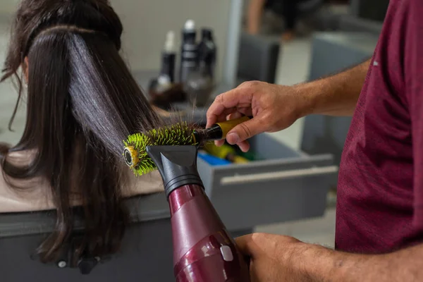 Detail of a hairdresser using a brush and dryer, brushing and drying a client\'s hair.